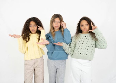 Foto de Tres jóvenes hermosas niñas multirraciales confundidas y molestas con la palma abierta que muestra espacio para copiar y señalar con el dedo a la frente. Piénsalo.. - Imagen libre de derechos