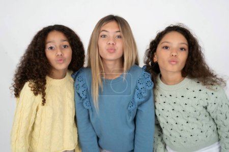 Foto de Disparo de aspecto agradable Tres chicas jóvenes hermosas multirraciales niños pucheros labios, mira a la cámara, expresiones faciales humanas - Imagen libre de derechos
