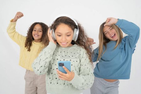 Foto de Feliz Tres jóvenes hermosas niñas multirraciales se siente bien mientras se centra en la pantalla del teléfono inteligente. Personas, tecnología, estilo de vida - Imagen libre de derechos