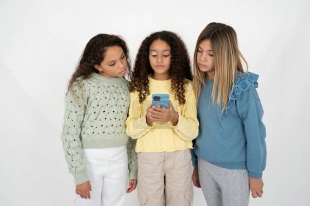 Foto de Enfocado Tres chicas jóvenes hermosas y multirraciales usan teléfonos inteligentes leyendo noticias de redes sociales o correos electrónicos importantes - Imagen libre de derechos
