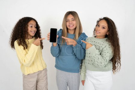 Foto de Atractivo alegre Tres jóvenes hermosas muchachas del niño multirracial sosteniendo en la célula de las manos que muestra la pantalla negra - Imagen libre de derechos