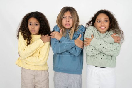 Desperate Three young beautiful multiracial kid girls trembles and feels cold, hugs oneself to warm up or feels scared notices something terrifying.