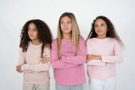 Photo for Charming thoughtful Three young beautiful multiracial kid girls stands with arms folded concentrated somewhere with pensive expression thinks what to do - Royalty Free Image