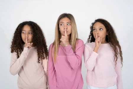 Téléchargez les photos : Trois belles jeunes filles multiraciales silence geste garde index aux lèvres fait signe de silence. Demande de ne pas partager le secret - en image libre de droit