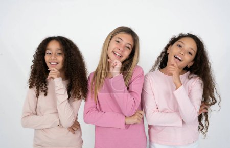 Foto de Tres jóvenes hermosas niñas multirraciales ríe felizmente mantiene la mano en la barbilla expresa emociones positivas sonríe ampliamente tiene expresión despreocupada - Imagen libre de derechos