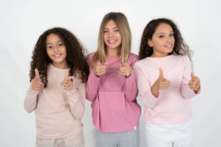 Foto de Tres jóvenes hermosas niñas multirraciales niños dirige los dedos a la cámara selecciona a alguien. Te recomiendo. La mejor opción - Imagen libre de derechos
