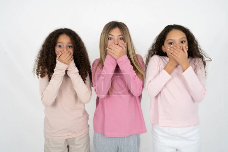 Stunned Three young beautiful multiracial kid girls covers both hands on mouth, afraids of something astonishing