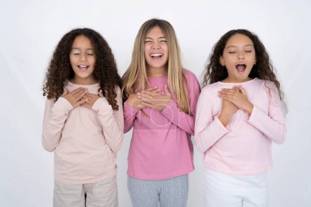 Téléchargez les photos : Trois belles jeunes filles multiraciales expriment leur bonheur, rient agréablement, gardent la main sur le cœur - en image libre de droit