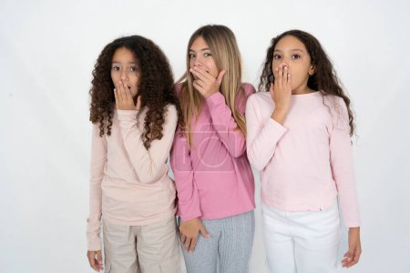 Foto de Tres jóvenes hermosas niñas multirraciales cubre la boca y mira con asombro a la cámara, no puede creer rumores inesperados. - Imagen libre de derechos