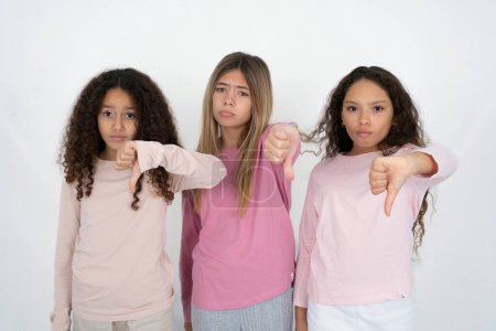 Foto de Tres chicas jóvenes hermosas y multirraciales que parecen infelices y enojadas mostrando rechazo y negativo con el gesto de los pulgares hacia abajo. Mala expresión. - Imagen libre de derechos