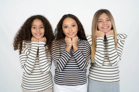 Téléchargez les photos : Satisfait Trois jeunes belles filles multiraciales enfant touche menton avec les deux mains, sourit agréablement, se réjouit bonne journée avec amant - en image libre de droit