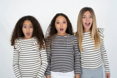 Foto de Sorprendido Tres jóvenes hermosas niñas multirraciales mira fijamente ojos con micrófonos mantiene la boca abierta ha sorprendido a la expresión. Concepto de Omg - Imagen libre de derechos