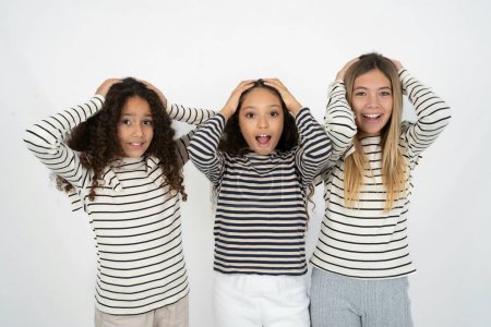 Photo for Cheerful overjoyed Three young beautiful multiracial kid girls reacts rising hands over head after receiving great news. - Royalty Free Image