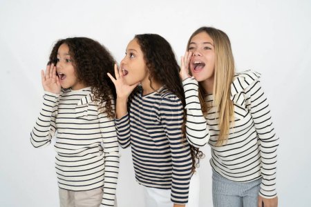 Photo for Three young beautiful multiracial kid girls look empty space holding hand face and screaming or calling someone. - Royalty Free Image