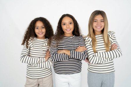 Photo for Portrait of charming Three young beautiful multiracial kid girls standing confidently smiling toothily with hands folded - Royalty Free Image