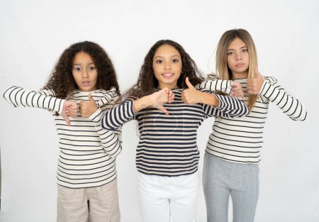 Tres jóvenes hermosas niñas multirraciales mostrando el pulgar hacia abajo signo