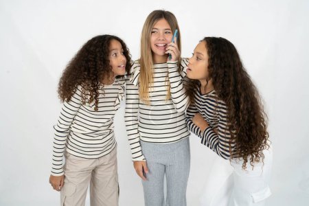 Foto de Feliz alegre encantador Tres jóvenes hermosas niñas multirraciales hablan hablan teléfono sonrisa buen humor - Imagen libre de derechos