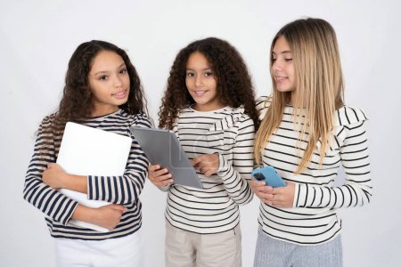 Téléchargez les photos : Photo de heureux gai Trois jeunes belles filles multiraciales enfant tiennent tablette navigation sur Internet - en image libre de droit