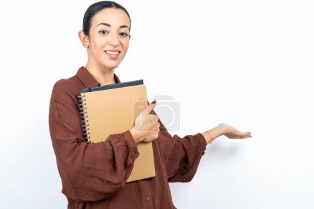 beautiful woman arab student carries notebooks with paper feeling happy and cheerful, smiling and welcoming you, inviting you in with a friendly gesture