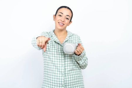 Photo for Beautiful young woman wearing green plaid pyjama and holding a cup pointing at camera with a satisfied, confident, friendly smile, choosing you - Royalty Free Image