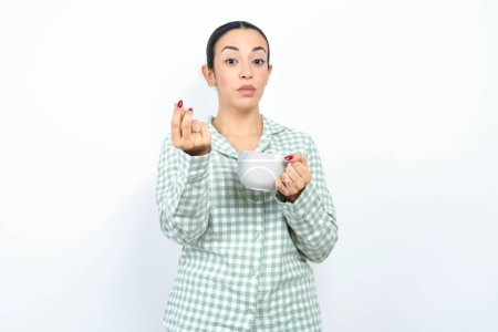 Photo for Beautiful young woman wearing green plaid pyjama and holding a cup doing money gesture with hands, asking for salary payment, millionaire business - Royalty Free Image