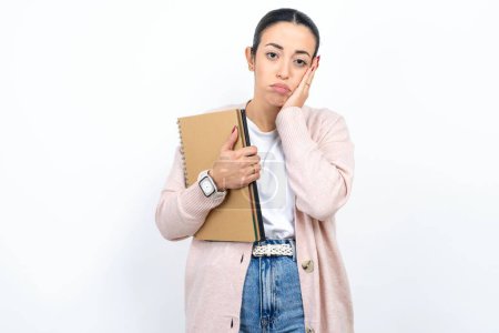 Téléchargez les photos : Belle étudiante arabe porte des carnets sur fond blanc mains fatiguées couvrant le visage, la dépression et la tristesse, bouleversé et irrité par le problème - en image libre de droit