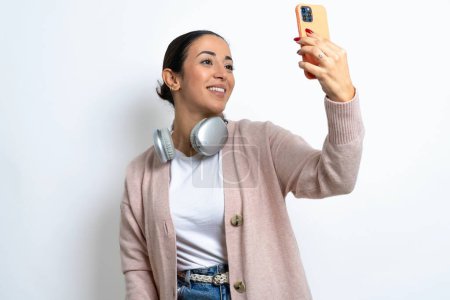 Téléchargez les photos : Belle femme arabe sur fond blanc souriant et prenant un selfie prêt à le poster sur ses médias sociaux. - en image libre de droit