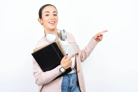 Téléchargez les photos : Belle étudiante arabe porte des cahiers sur fond blanc point à copyspace recommander des réductions de vente - en image libre de droit