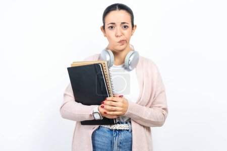 Beleidigt unzufrieden schöne arabische Studentin trägt Notizbücher über weißem Hintergrund mit launisch missmutiger Miene in die Kamera enttäuscht von etwas