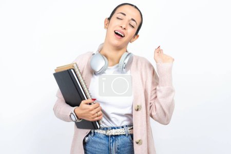 Téléchargez les photos : Joyeux succès belle arabe étudiante porte des carnets sur fond blanc soulève la paume et ferme les yeux dans la joie d'être diverti par des amis - en image libre de droit