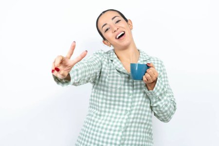 Foto de Hermosa mujer joven con pijama a cuadros verdes y sosteniendo una taza dirige los dedos a la cámara selecciona a alguien. Te recomiendo. La mejor opción - Imagen libre de derechos