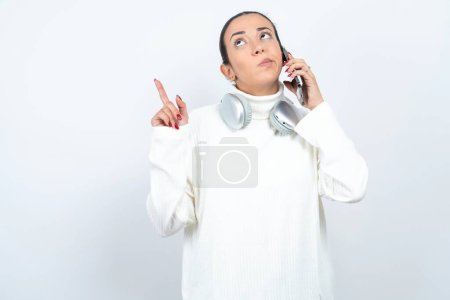 Téléchargez les photos : Belle femme arabe posant sur fond blanc parle sur téléphone mobile passe du temps libre à l'intérieur appels à un ami. - en image libre de droit