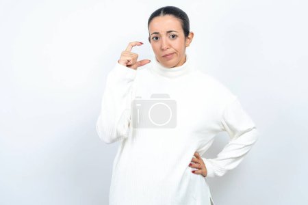 Foto de Mujer árabe hermosa descontenta posando sobre fondo blanco formas poco signo de mano demuestra algo no muy grande. Concepto de lenguaje corporal. - Imagen libre de derechos