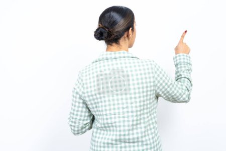 Téléchargez les photos : Belle jeune femme portant pyjama à carreaux vert sur fond blanc pointant vers l'objet sur l'espace de copie, vue arrière. Tourne le dos - en image libre de droit