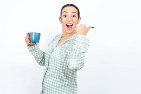 Photo for Hooray cool Beautiful young woman wearing green plaid pyjama and holding a cup point back empty space hand fist - Royalty Free Image