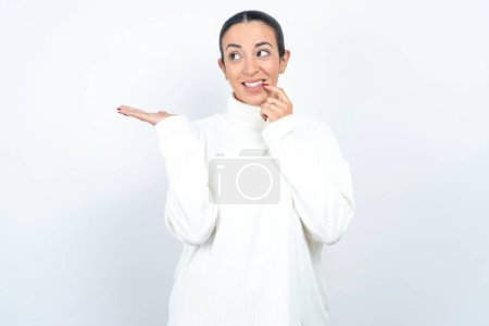 Foto de Positivo hermosa mujer árabe posando sobre fondo blanco anuncio promo toque dientes de dedo - Imagen libre de derechos