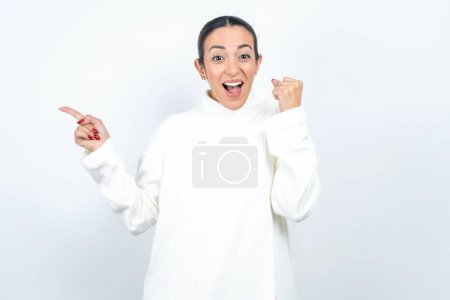 Foto de Hermosa mujer árabe posando sobre puntos de fondo blanco en el espacio vacío sosteniendo el puño hacia arriba, gesto ganador. - Imagen libre de derechos