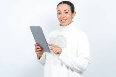 Téléchargez les photos : Photo de heureux joyeux smart belle femme arabe posant sur fond blanc tenir tablette navigation sur Internet - en image libre de droit
