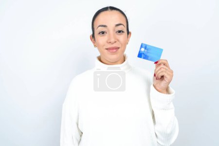 Foto de Foto de feliz alegre sonriente positiva hermosa mujer árabe posando sobre fondo blanco recomiendan tarjeta de crédito - Imagen libre de derechos