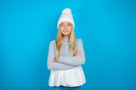 Dreamy rest relaxed Beautiful kid girl wearing white knitted hat and blue sweater crossing arms,