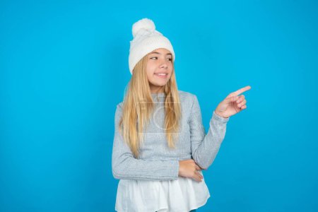 Photo for Photo of attractive Beautiful kid girl wearing white knitted hat and blue sweater direct finger empty space cheap dentistry - Royalty Free Image