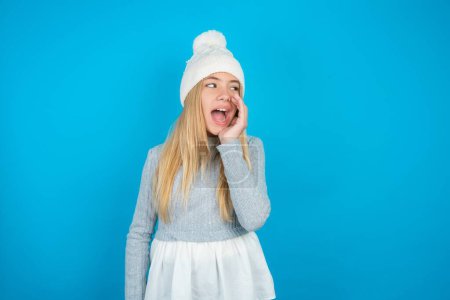 Beautiful kid girl wearing white knitted hat and blue sweater hear incredible private news impressed scream share