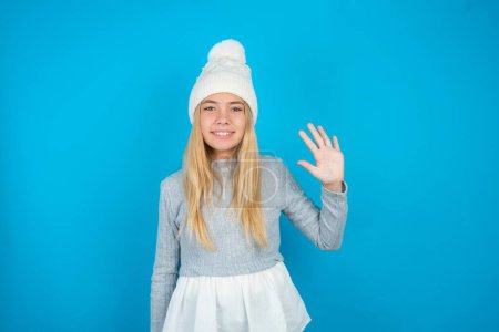 Photo for Beautiful kid girl wearing white knitted hat and blue sweater showing and pointing up with fingers number five while smiling confident and happy. - Royalty Free Image