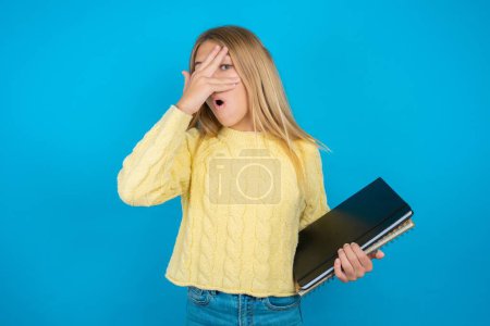 Photo for Beautiful kid girl wearing yellow sweater peeking in shock covering face and eyes with hand, looking through fingers with embarrassed expression. - Royalty Free Image