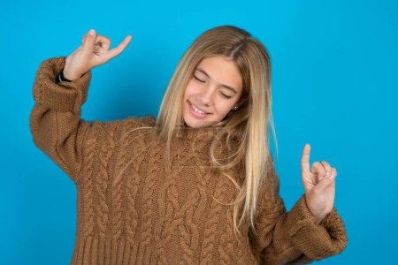 Téléchargez les photos : Photo de optimiste Belle jeune fille portant un pull en tricot marron s'amuse et danse vêtements insouciants être d'humeur parfaite fait des mouvements. Passe du temps libre sur disco partie - en image libre de droit