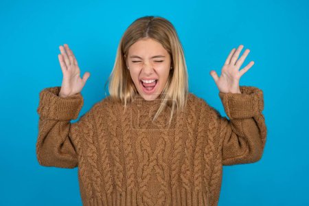 Beautiful kid girl wearing brown knitted sweater goes crazy as head goes around feels stressed because of horrible situation