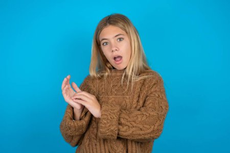 Photo for Surprised emotional Beautiful kid girl wearing brown knitted sweater rubs palms and stares at camera with disbelief - Royalty Free Image