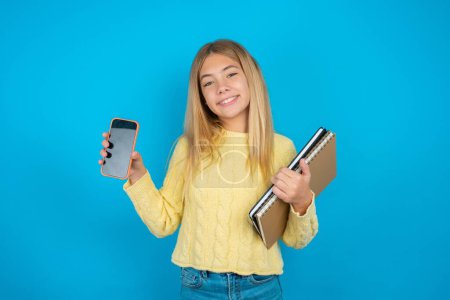 Foto de Hermosa niña con suéter amarillo Mostrar teléfono inteligente pantalla en blanco, pulgar hacia arriba recomiendan nueva aplicación - Imagen libre de derechos