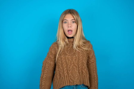 Photo for Shocked Beautiful kid girl wearing brown knitted sweater stares bugged eyes keeps mouth opened has surprised expression. Omg concept - Royalty Free Image