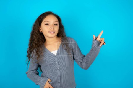 Téléchargez les photos : Belle fille enfant portant une veste décontractée sur fond bleu regardant la caméra indiquant les ventes d'espace vide doigt - en image libre de droit